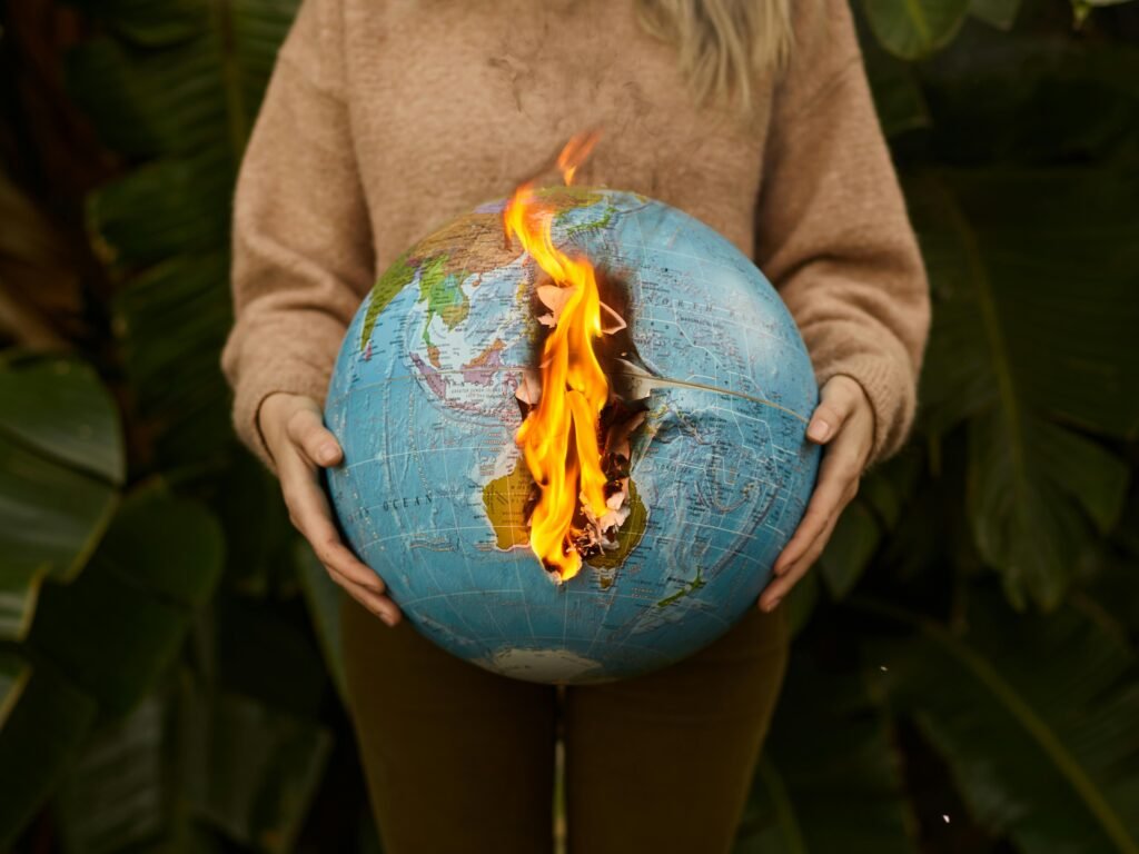 A symbolic portrayal of climate change with a burning globe held in hands, set against a nature background.