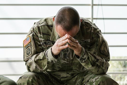 A soldier in camouflage sitting indoors, appearing stressed and overwhelmed.